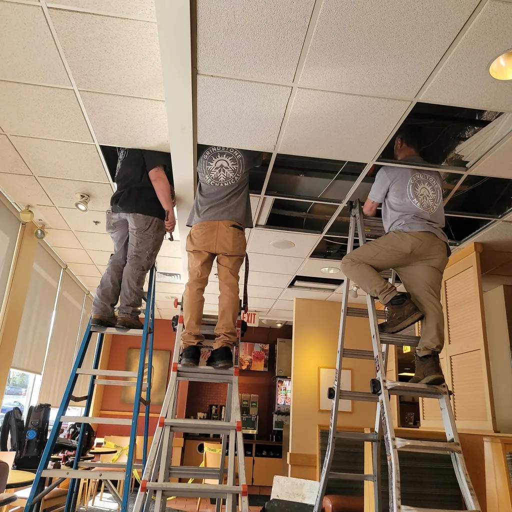 Three technicians on ladders working in the open ceiling of a restaurant.