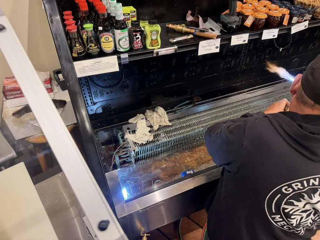 Technician brazing copper refrigeration lines on top of a grocery refrigerated case.