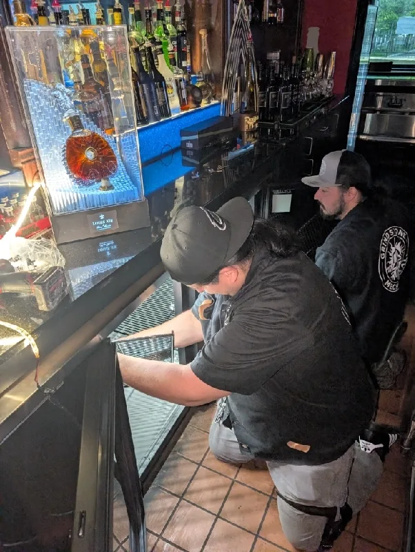 Technician reaching into an open glass-door bar cooler.