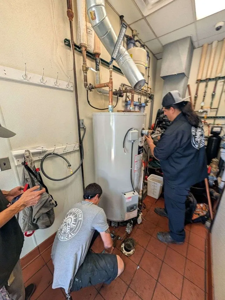 Two technicians installing a tall white commercial water heater in a kitchen.