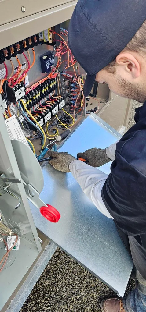 Close-up of gloved hands wiring a dense HVAC control panel.