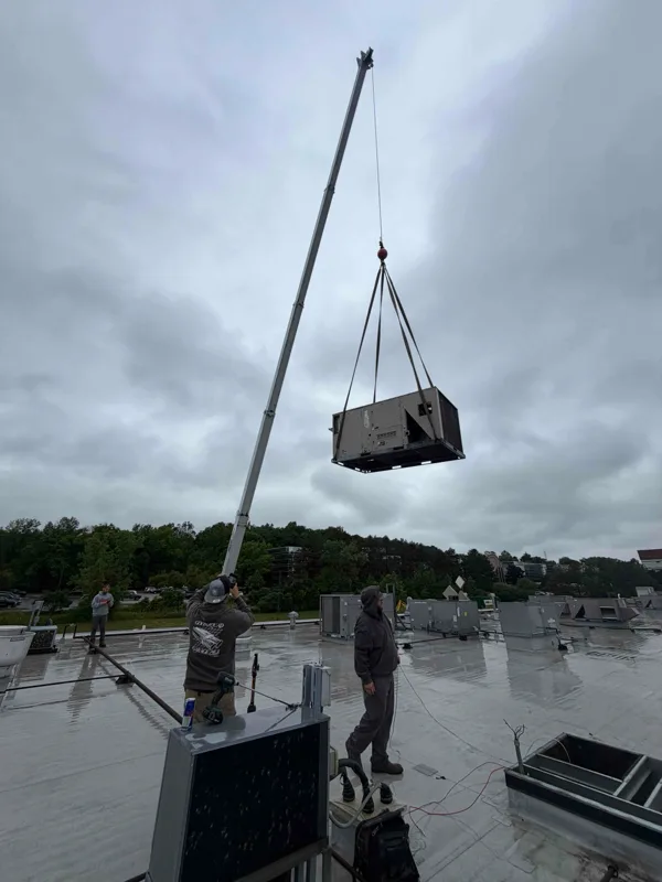 Technician pressure-washing a condenser coil on a gravel roof, with the Grindstone van below.