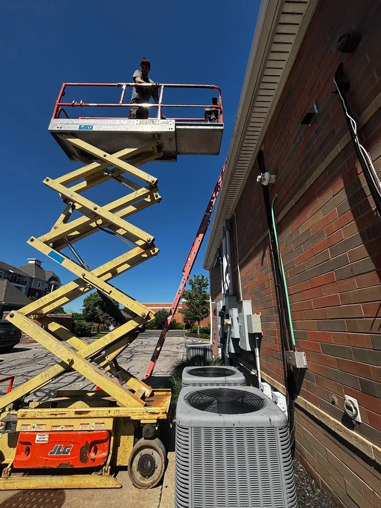 Scissor lifts raised beside outdoor condenser units at a brick commercial building.