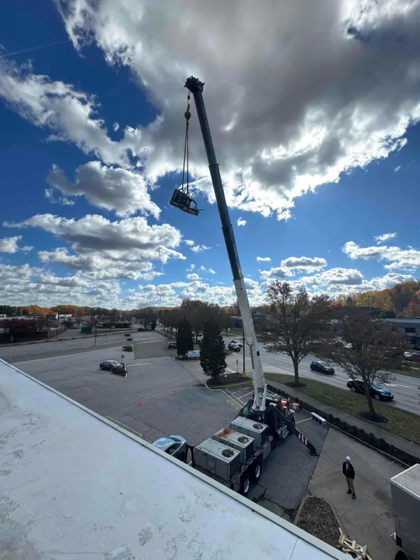 Crane lifting a rooftop unit over an autumn parking lot.