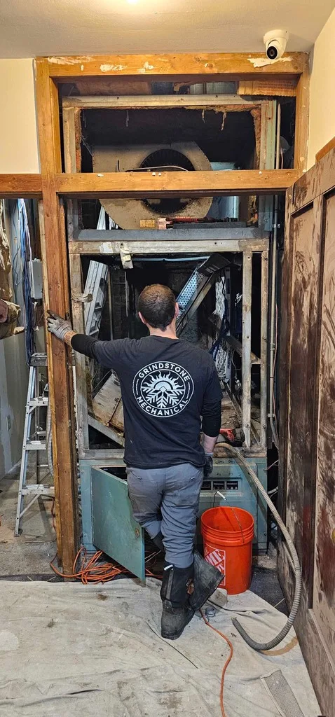 Technician in a Grindstone shirt rebuilding a large air handler with its panels open.