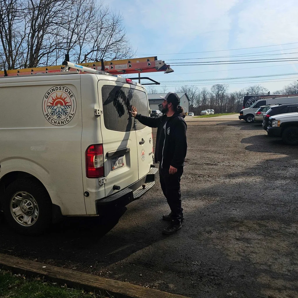 White Grindstone Mechanical service van with the gold sunburst logo, parked by picnic tables.