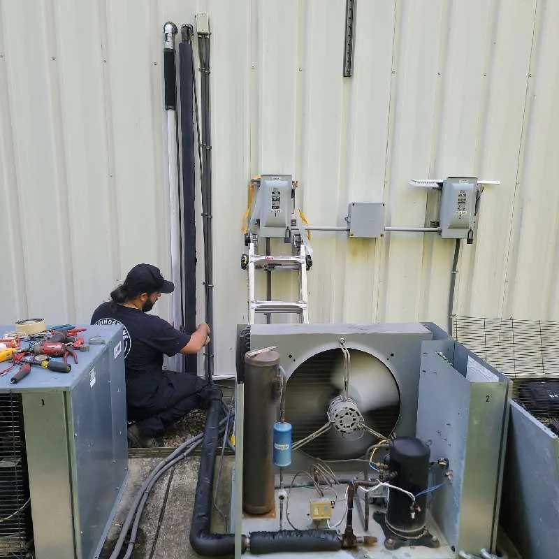 Gloved hands working on refrigeration condensing units mounted on a wall.